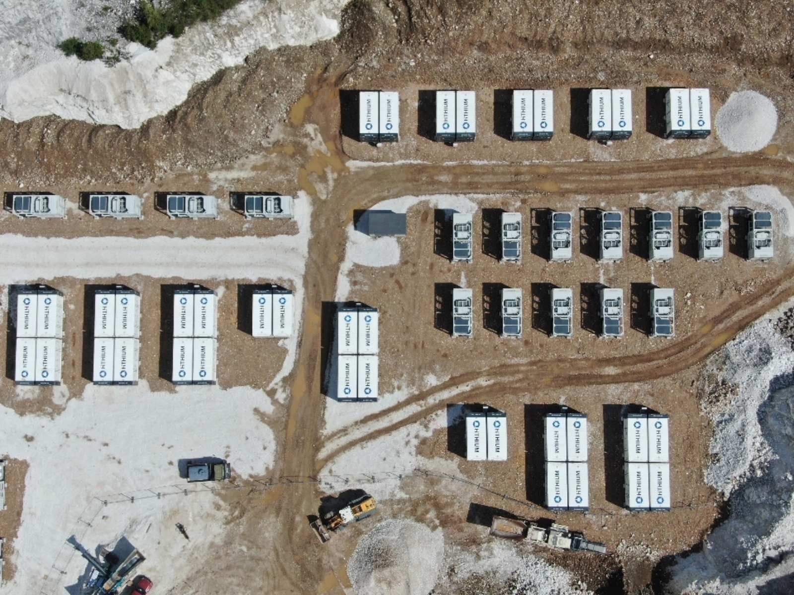 Wide aerial view of the operational Project Jupiter battery storage system, with rows of Hithium containers and the substation pad nestled within the surrounding quarry walls and forest.